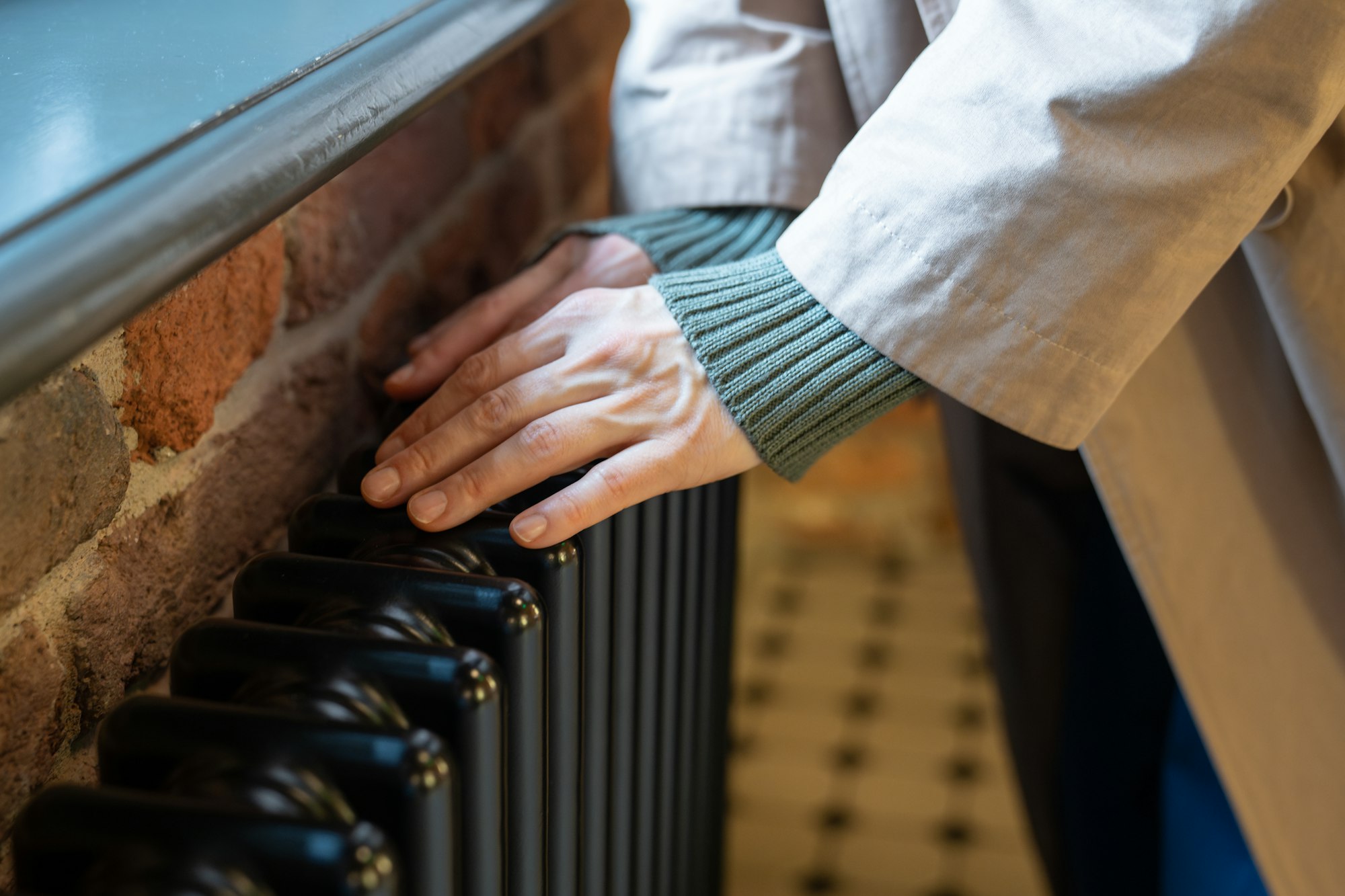 Woman warming hands near old vintage radiator at home, checking heating system working capacity